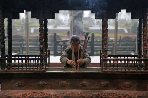 Una de las residentes acogidas por Neng Qing coloca barras de incienso en el templo de Ji Xiang. (Foto: BBC)